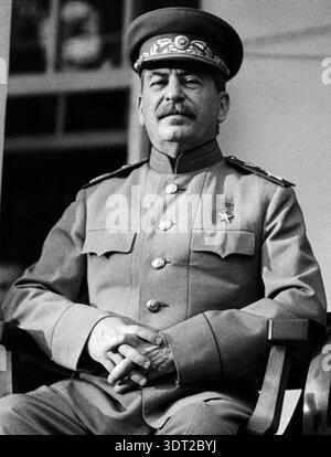Dieses beeindruckende Schwarzweiß-Foto aus dem Jahr 1943 zeigt Joseph Stalin, den damaligen Premierminister der Sowjetunion, sitzend und direkt in die Kamera blickend. Er trägt Militäruniform, mit Medaillen und einer verzierten Mütze, während einer wichtigen Kriegskonferenz. Stockfoto