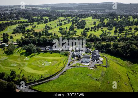 Eine hochwinklige Drohnenaufnahme zeigt eine Ansammlung moderner Steingebäude, umgeben von einem gepflegten grünen Golfplatz. In der Landschaft gibt es Fairways, Bunker Stockfoto