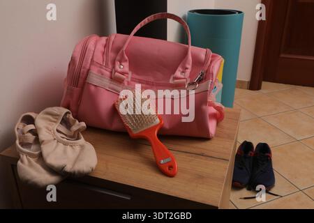 Ballettschuhe, eine Haarbürste, eine pinkfarbene Sporttasche und Turnschuhe auf Holzoberfläche Stockfoto