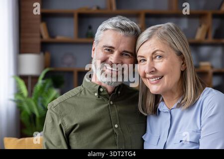 Ein lächelndes reifes Paar zu Hause, das eine warme Umarmung teilt und Liebe, Zufriedenheit und Gesellschaft in ihrem entspannten Alltag und in ihrem gemeinsamen Ruhestand ausstrahlt Stockfoto