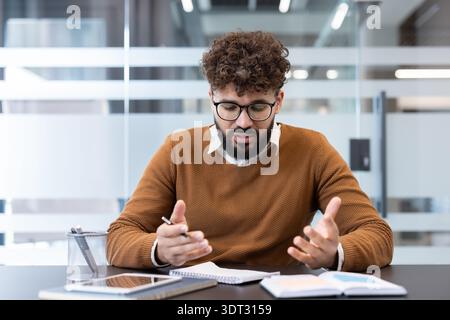 Nachdenklicher junger Geschäftsmann, der Ideen entwickelt und diskutiert, mit einem Notizbuch und Stift, während er aktiv an einem kreativen Brainstorming-Sessio teilnimmt Stockfoto