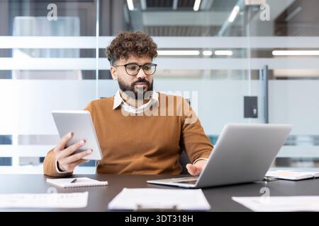 Junge Profis, die an einem modernen Schreibtisch arbeiten, Multitasking mit Laptop und Tablet durchführen und sich auf digitale Tools für Produktivität, Planung und Analyse konzentrieren Stockfoto