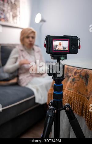 Seniorin erstellt Inhalte als Influencer und nimmt einen Video-Blog mit ihrer Kamera in einem Heimstudio auf Stockfoto