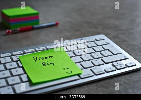 Grüne Haftnotiz „Dream Big“ auf der Tastatur. Der helle Ton hebt sich von den Tasten ab und symbolisiert Motivation und Produktivität. Stockfoto