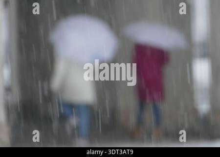 Zwei Frauen gehen mit Regenschirmen im starken Regen. Abstraktes unscharfes Wetterbild, das Freundschaft, Zusammenhalt, Melancholie und den Umgang mit Krisen symbolisiert. Stockfoto