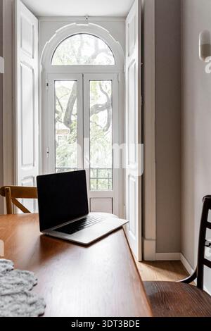 Laptop auf einem Holztisch in einem hellen Innenraum in der Nähe offener Glastüren, mit Tageslicht in den Raum Stockfoto
