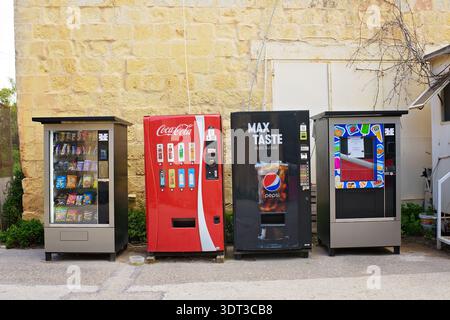 Gzira, Malta - 17. Februar 2026: Eine Reihe verschiedener Automaten mit Snacks, Coca-Cola und Pepsi-Getränken stehen an einer Steinmauer. Stockfoto