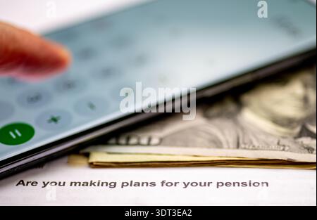 Eine Makroaufnahme von US-Dollar-Rechnungen und ein Telefonrechner auf einem Rentenbrief. Ein Pensionsplan-Konzept. Stockfoto