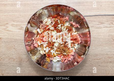 Hackfleisch, gehackte Zwiebeln, zwei rohe Eier und Gewürze in einer Metallschüssel, fertig zum Kochen Stockfoto