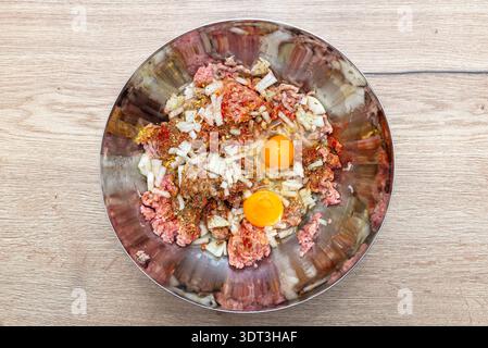 Hackfleisch, gehackte Zwiebeln, zwei rohe Eier und Gewürze in einer Metallschüssel, fertig zum Kochen Stockfoto