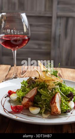 Erstklassiger Caesar-Salat mit gegrilltem Huhn, Wachteleiern und Parmesan-Chisps kombiniert mit einem Glas Rotwein; ein kulinarisches Erlebnis für alle Sinne Stockfoto