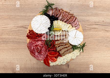 Serviert wird eine runde Holzplatte mit verschiedenen Aufschnitt-, Käse- und Beilagen Stockfoto