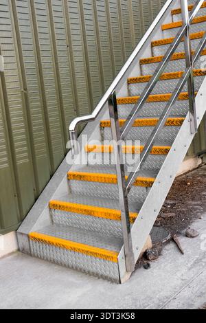 Eine industrielle Metalltreppe mit Stahlstufen aus Schachtschild. Jede Stufe ist mit einem gut sichtbaren gelben, rutschfesten Treppenstufenprofil ausgestattet. Stockfoto