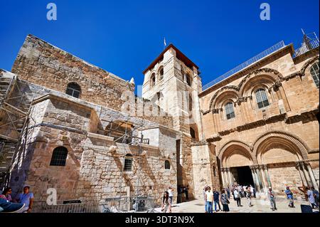Besucher versammeln sich um die Grabeskirche in Jerusalem. Die Sonne scheint hell, während die Menschen die historische Stätte und ihre Architektur erkunden. Stockfoto
