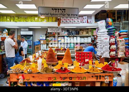 Die Leute kaufen Gewürze auf dem Mahane Yehuda Markt in Jerusalem. Bunte Gewürze werden in Stapeln auf dem Theken ausgestellt. Stockfoto