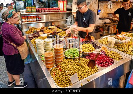 Auf dem Mahane Yehuda Market in Jerusalem können Besucher frische Oliven und lokale Gerichte genießen. Verkäufer bieten Kunden eine Vielzahl von Oliven und Snacks an. Stockfoto