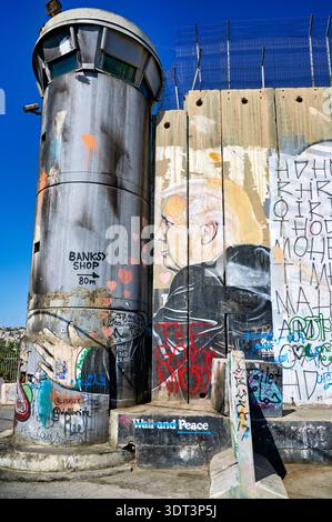 Die Szene zeigt die Trennwand in Bethlehem mit Wachturm und Straßenkunst. Graffiti bedecken die Wand und drücken verschiedene Botschaften aus. Stockfoto