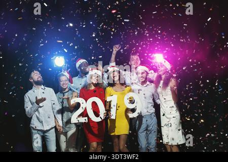Große Gruppe von Freunden feiert Silvester mit Konfetti und Lächeln im Jahr 2019 Stockfoto