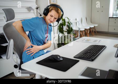 Weibliche Callcenter-Agentin mit starken Rückenschmerzen Stockfoto