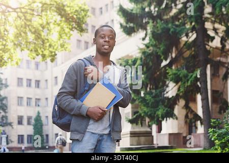 Junger Mann steht mit Büchern auf dem Campus im Sonnenlicht am Nachmittag Stockfoto