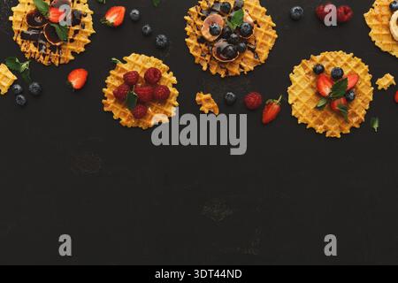 Waffeln in einer kreativen Collage mit Früchten und Belägen auf dunklem Hintergrund Stockfoto