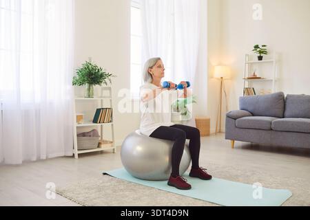 Active Fit alte sportliche Seniorin, die mit Fitnessball trainiert, Hanteln zu Hause, Sport macht Stockfoto