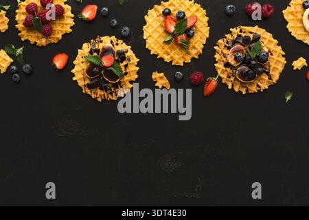 Sammlung von Waffeldesserts mit Früchten und Belägen auf einer dunklen Oberfläche bei einer Versammlung Stockfoto