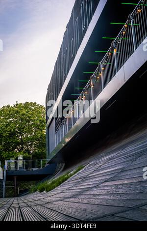 Eine dynamische, flache Aufnahme eines beeindruckenden modernen Gebäudes mit schwarzer Fassade und einem einzigartigen geschwungenen Holzsteg oder einer Rampe. Das elegante Metallgeländer Stockfoto