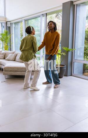 Verschiedene Paare tanzen auf Fliesen in einem modernen Wohnzimmer mit Glaswänden, legeren Kleidern und Pflanzen Stockfoto