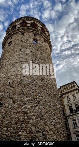 Niedrigwinklige Ansicht des historischen Galata-Turms mit strukturierten Steinmauern vor einem dramatischen bewölkten Himmel in Istanbul, Türkei Stockfoto
