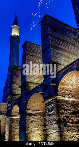 Beleuchtetes Minarett, byzantinische Strebepfeiler und Ramadan-Mahya-Lichter an der Außenseite der Hagia Sophia zur Blauen Stunde in Istanbul, Türkei. Stockfoto