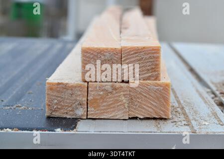 Eine horizontale Nahaufnahme mehrerer quadratischer Holzbalken, die auf einer Metallfläche gestapelt sind. Das Bild zeigt deutlich die natürliche Holzmaserung und Säge Stockfoto