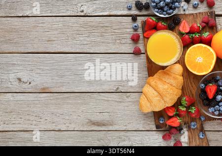 Frühstück mit Obst, Croissants und Saft auf Holztisch mit leerem Platz Stockfoto
