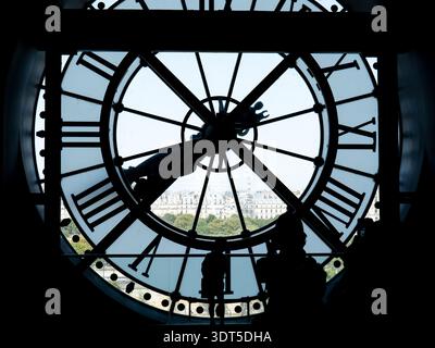 Die Silhouette der Besucher, die durch die riesige historische Uhr mit Blick auf die Skyline von Paris gesehen werden, schafft ein künstlerisches Reisekonzept von Zeittourismus und Kultur Stockfoto