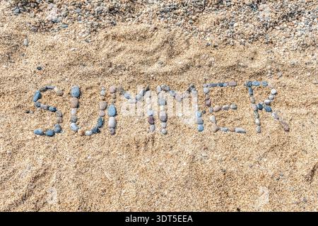 Direkter Blick von oben auf das Wort SOMMER handgefertigt aus natürlichen Meereskieseln an einem sonnigen Sandstrand. Kreative flache Komposition mit Kopierraum Stockfoto