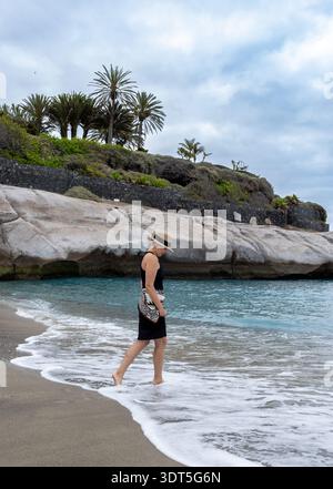 Stilvolle Frau, Die Barfuß Am Tropical Beach Mit Rocky Cliff Und Palm Landscape Spaziert Stockfoto