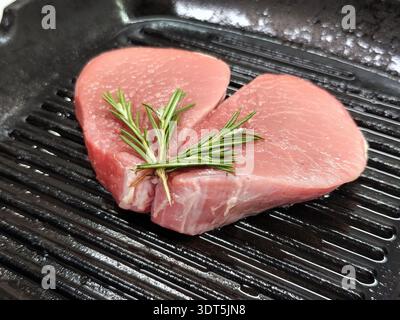 Zwei rohe Fleischsteaks in Herzform auf einer Grillpfanne mit Rosmarin. Blick von oben auf frisches, ungekochtes Rindfleisch mit Kräutern, romantisches Essenskonzept. Stockfoto