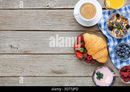 Genießen Sie das Frühstück mit Kaffee, Croissants, Obst und Joghurt auf einem Holztisch Stockfoto