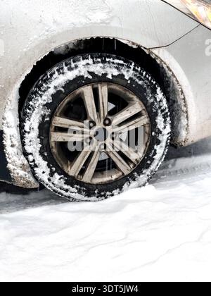 Nahaufnahme eines schmutzigen Autorads mit Alufelge und Winterreifen mit Schnee. Fahrzeug auf schneebedecktem Boden geparkt, sichtbares Profil, Eis, Slush, Stockfoto