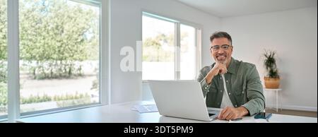 Ein glücklicher älterer Mann mittleren Alters, der einen Laptop am Heimtisch benutzt. Hochformat Stockfoto