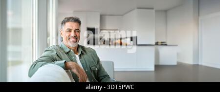 Porträt eines glücklichen Mannes mittleren Alters, der zu Hause auf der Couch sitzt und in die Kamera schaut. Stockfoto