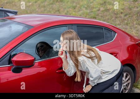 Eine Frau, die Lippenstift aufträgt. Eine Frau, die aus einem Autofenster schaut. Ein besorgter Fahrer. Fahrzeugkonzept. Stockfoto