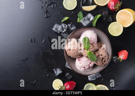 Verschiedene Geschmacksrichtungen von Eis serviert mit Früchten und Eis auf einer schwarzen Oberfläche Stockfoto