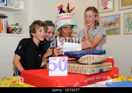 Mann feiert seinen 50. Geburtstag zu Hause mit seinen Kindern, lächelt um Geschenke und Geburtstagskuchen, Familie Lifestyle Porträt. Stockfoto