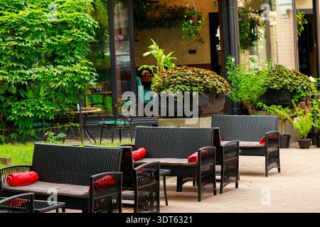 Ein ruhiger Sitzbereich im Freien in einem Café, geschmückt mit lebendigen Pflanzen und stilvollen Korbmöbeln, lädt zur Entspannung und Unterhaltung ein Stockfoto