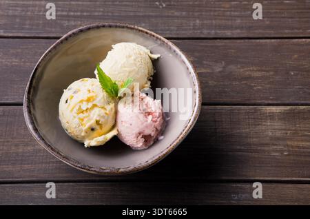 Drei Kugeln Eiscreme in einer Schüssel auf einem Holztisch Stockfoto