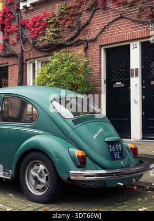 Amsterdam, Niederlande - 21. Oktober 2024: Grüner Volkswagen Käfer, der auf einer Straße vor einem Backsteinhaus mit leuchtendem rotem Autoton geparkt ist Stockfoto