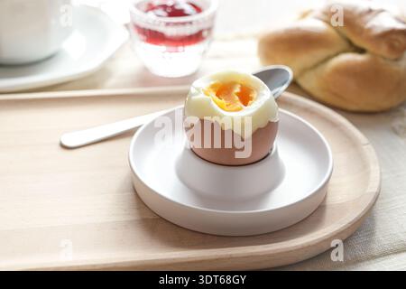Geöffnetes gekochtes Ei mit weichem Eigelb in einem Eierbecher auf einem Holzteller, köstliches Protein zum Frühstück, Brunch oder Mittagessen, Kopierraum, ausgewählter Fokus, narro Stockfoto