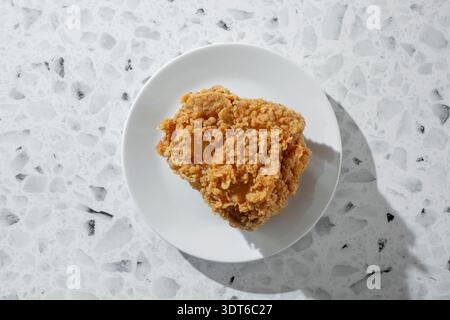 Ein Blick von oben nach unten auf einen extra knusprigen, gebratenen Hähnchenschenkel, auf einem Teller. Stockfoto