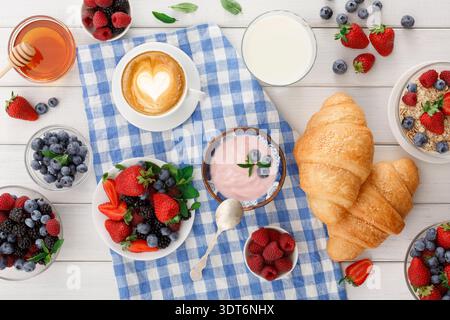 Frühstück mit Obst, Joghurt, Kaffee und Croissants auf einer karierten Tischdecke Stockfoto